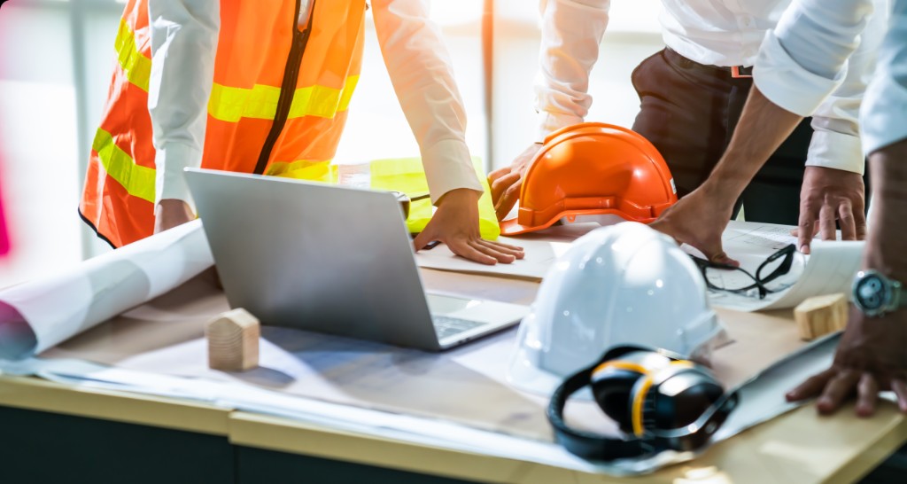 Construction team reviewing plans around a table with hard hats and a laptop